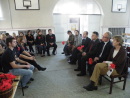Na zdęciu znajduje sie grupa ludzi siedzących na przeciwko siebie i rozmawiających