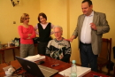 Na zdjeciu z wizyty znajduje sie kilkoro ludzie. Jeden mężczyzna siedzi przed notebookiem, a drugi stoi obok i tłumaczy. W tyle 2 kobiety.