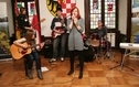 <p>Zespół "Kościuszkowcy". Na zdjeciu gra zespł składający się z pięciu osób. Śpiewa młoda kobieta.</p>