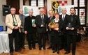 <p>Laureaci Kryształów. Na zdjęciu grupa ludzi. Sześciu mężczyzn, jeden ksiądz i jedna kobieta z kwiatami. Wszyscy trzymają nagrody.</p>