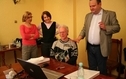<p>Na zdjeciu przed komputerem siedzi meżczyzna podłaczony do laptopa od uszu przewodami, obok stoi i drugi i tłumaczy a w tyle dwie kobiety sie przyglądają.</p>