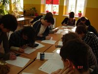 Na zdjęciu młodzi ludzie dziewczyny i chłopcy przy stole w klasie rozwiązują zadania matematyczne